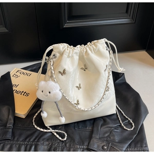 Detail van witte bucket bag met zilveren vlinderbedeltjes en een kettingriem