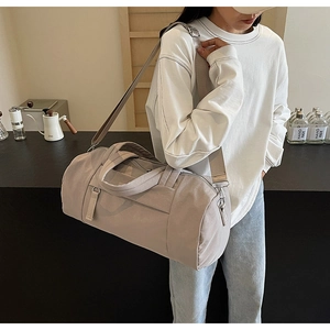 Primer plano de un bolso cilíndrico gris claro minimalista con correa de hombro tejida