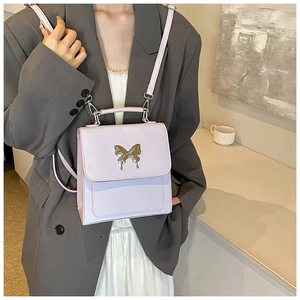 Détail d'un sac bandoulière lilas avec fermoir papillon doré porté sur un blazer gris