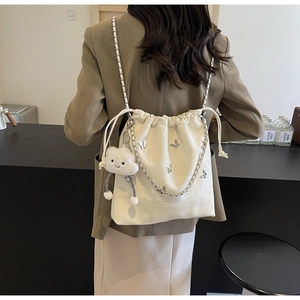 Detail van de crèmekleurige bucketbag met vlinderborduurwerk en wolkhanger