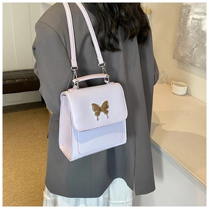 Détail du sac à main violet clair texturé avec un ornement de papillon doré élégant