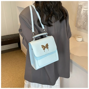 Sac à bandoulière bleu clair en cuir avec fermoir papillon doré porté par un modèle