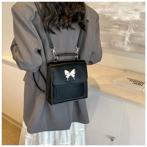 Détail d'un sac à dos en cuir PU noir avec un ornement papillon en métal argenté liquide