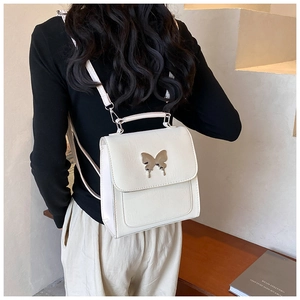 Détail d'un sac à dos blanc avec papillon argenté posé sur un banc en bois
