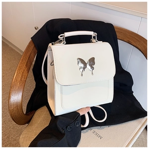 Détail d'un sac à main blanc structuré avec boucle papillon argentée sur fond noir