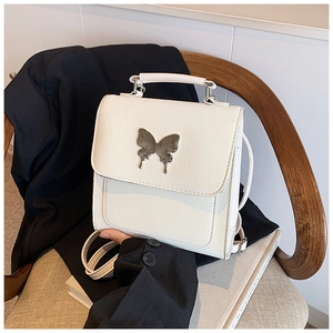 Détail d'un mini sac à dos blanc avec papillon en métal argenté sur un costume noir