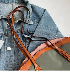 Detail of army green canvas tote with brown leather handles on a denim jacket