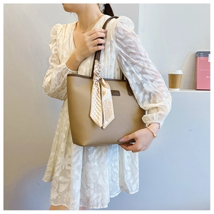 Detail view of khaki pebbled tote bag with brown handles and elegant printed scarf accessory