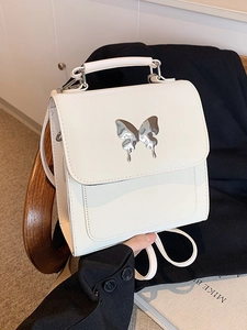 Sac à main carré blanc avec boucle papillon argentée posé sur un blazer noir élégant