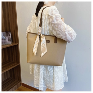Detail of light brown leather tote bag with elegant silk scarf on handle and branded label