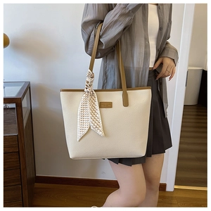 Detail of cream tote bag with brown handles and a patterned silk scarf on the strap
