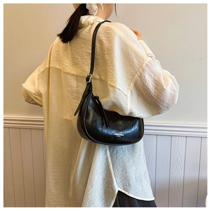 Détail d'un sac demi-lune en cuir noir avec bandoulière réglable et logo métallique