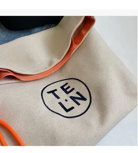 Detail of thick canvas tote with bright orange lining and navy TELN embroidery