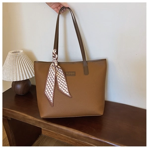 Detail of brown litchi grain leather tote bag with elegant silk scarf and metal logo