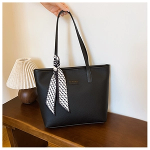 Close-up of black lychee grain tote bag with geometric scarf and metal brand plate