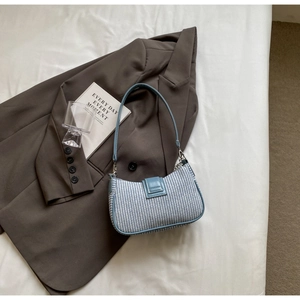 Détail du sac demi-lune tissé bleu et blanc sur un blazer gris avec accessoires