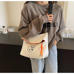 Close-up of cream canvas tote bag featuring orange trim and black adjustable strap
