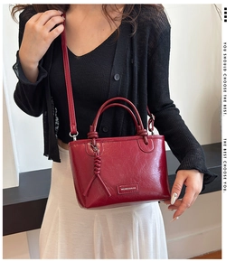 Détail d'un sac cabas rouge foncé avec texture brillante et pompon tressé pour femmes
