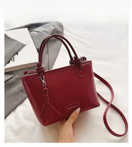 Détail du sac seau bordeaux avec poignée nouée, pendentif gland tressé et logo de la marque