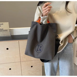 Detail of dark grey canvas tote bag featuring blue letter embroidery and orange lining
