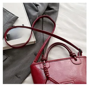 Vue détaillée du sac seau en cuir rouge vin brillant avec sa plaque logo métallique