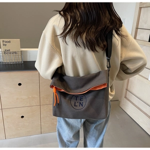 Detail of dark grey canvas tote bag featuring orange zipper and logo in crossbody view