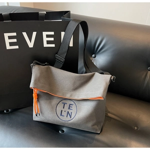 Detail of grey canvas crossbody bag with blue logo embroidery and orange zipper accents