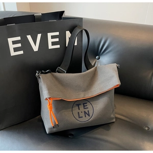 Close-up of gray canvas tote bag with orange lining on a black leather sofa