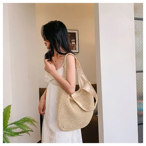 Detail of a large off-white straw tote bag with fine woven texture and wide shoulder strap