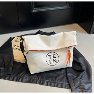 Detail of white canvas tote bag with orange zipper and embroidered logo on leather