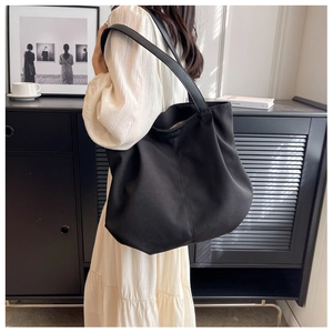 Side view of a large black canvas tote bag worn by a model in a minimalist room