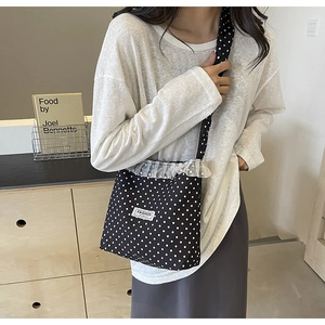 Close-up of black polka dot crossbody bag featuring white lace trim and fashion patch