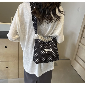 Dettaglio borsa a secchiello in nylon nero a pois con bordo in pizzo ed etichetta logo