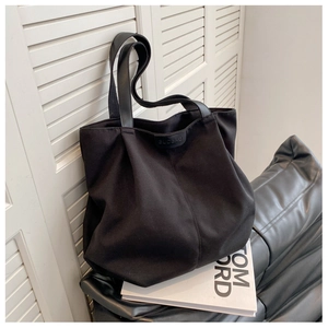 Macro view of black canvas tote bag showing the branded leather logo tag and texture