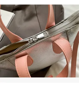 Detail of silver metallic leather handbag with pink handle and smooth metal zipper