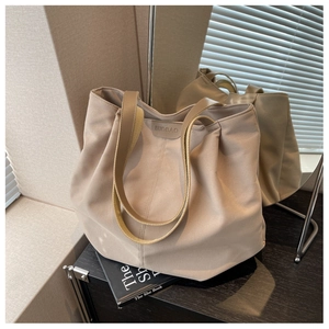 Close-up of the beige canvas tote bag with a leather brand logo and long handles