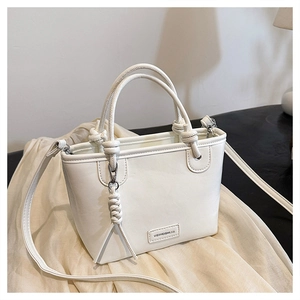 Détail d'un sac seau blanc en similicuir texturé avec un pendentif nœud tressé élégant
