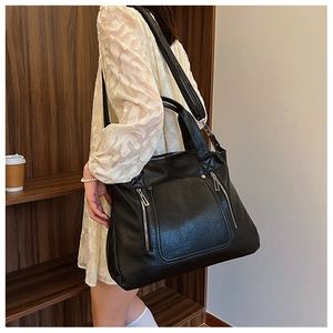 Detail of a large black faux leather tote bag with functional front metal zippers