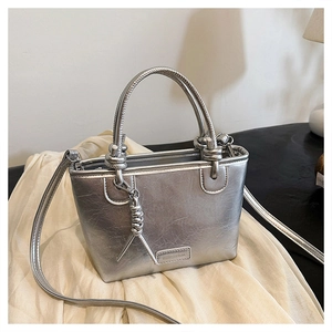 Détail d'un sac seau argenté métallisé avec poignées nouées et plaque signalétique