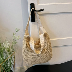 Detail of hollow-out straw woven tote bag with canvas strap hanging on a door handle