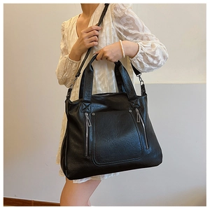Detail of black faux leather tote bag with silver decorative zippers and adjustable strap