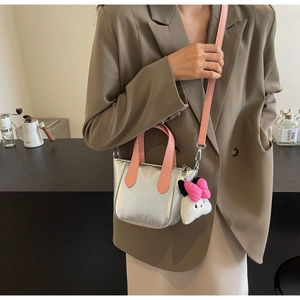 Detail of silver metallic handbag with pink straps and a cute plush charm on a suit