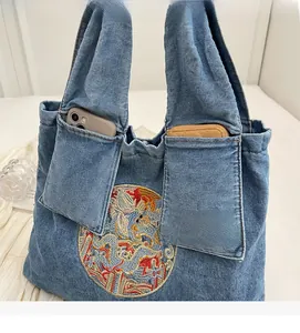 Détail d'un cabas en jean bleu avec broderie de dragon et poches plaquées sur le devant