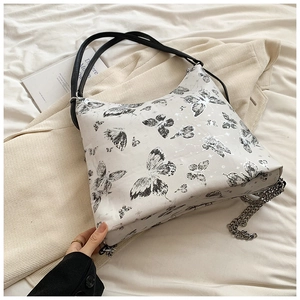 Close-up of white shoulder bag featuring black butterfly prints and silver chain detail