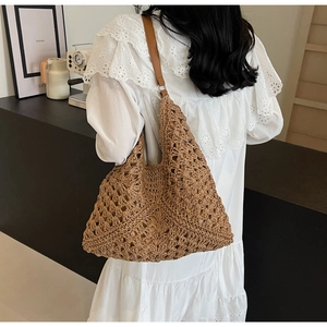 Detail of hollow woven pattern on brown straw tote bag with leather shoulder strap