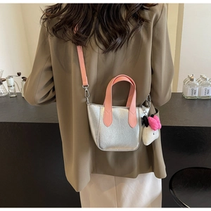 Detail of silver metallic handbag with pink handles and plush charm in a cafe setting