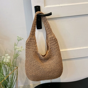Detailed close-up of handmade woven straw hobo bag hanging on a white wooden door handle