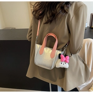 Detail of silver metallic bucket bag with pink handles and a plush bunny charm on model