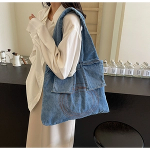 Detailed shot of large blue denim tote bag with red spiral embroidery on model