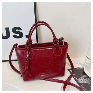 Détail d'un sac seau bordeaux avec des nœuds tressés et une plaque logo métallique